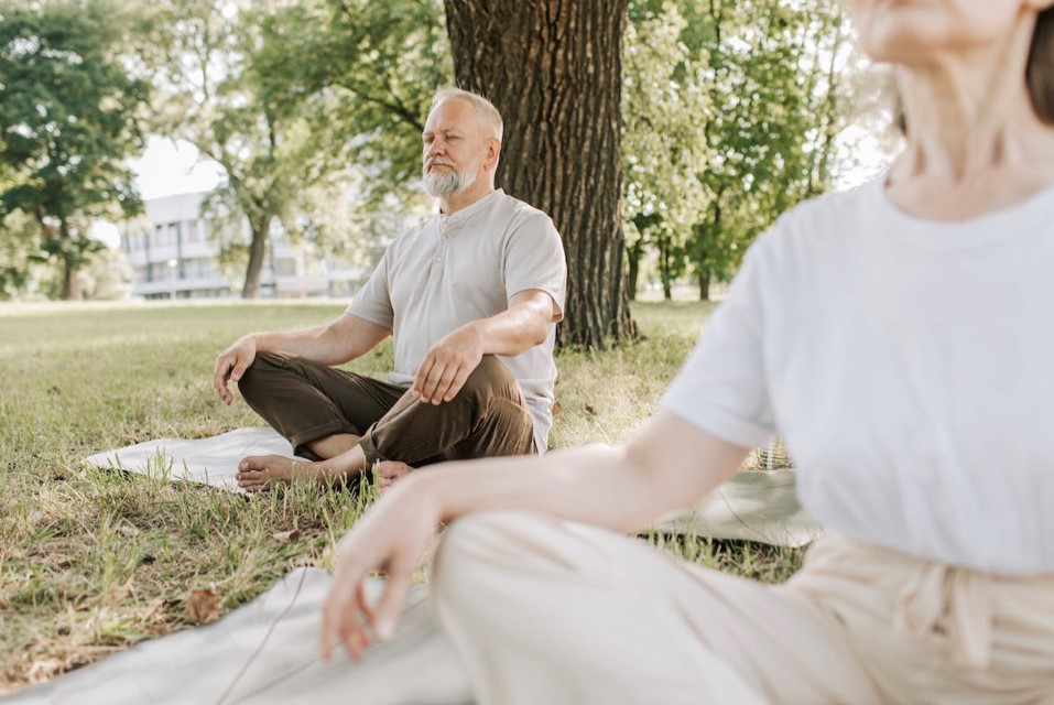 Ein Ehepaar sitzt gemiensam auf Yoga Matten im Wohnzimmer am Boden
                                                                                                                                    und dehnt sich. Sie bereiten sich auf ein Training vor.